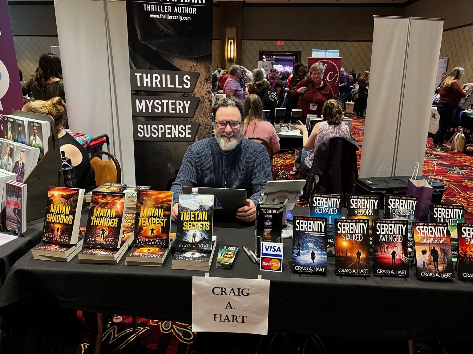 Craig A. Hart behind a conference table displaying his thriller novels